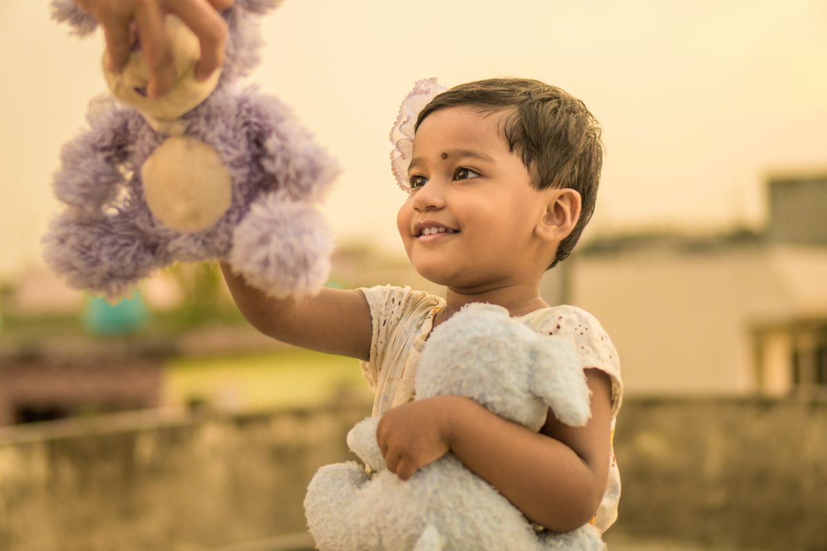 A smiling child joyfully plays with stuffed toys in an outdoor setting, capturing a moment of happiness.