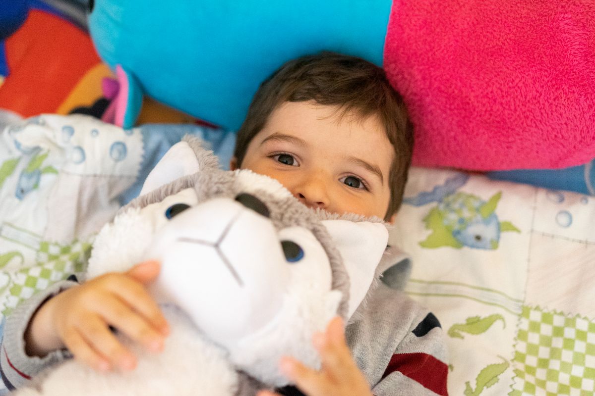 A cute child lying on a colorful bed, happily hugging a plush toy. Perfect capture of childhood joy.