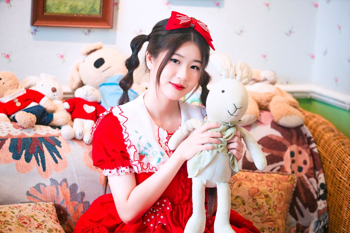 A young girl joyfully holding a plush rabbit toy in a cozy room filled with stuffed animals.