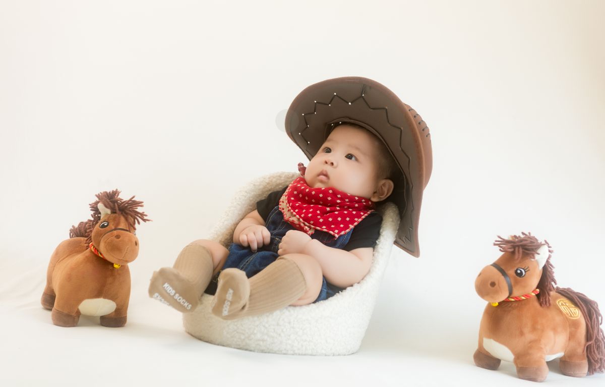 Charming baby in cowboy hat with plush horses, perfect for nursery decor.