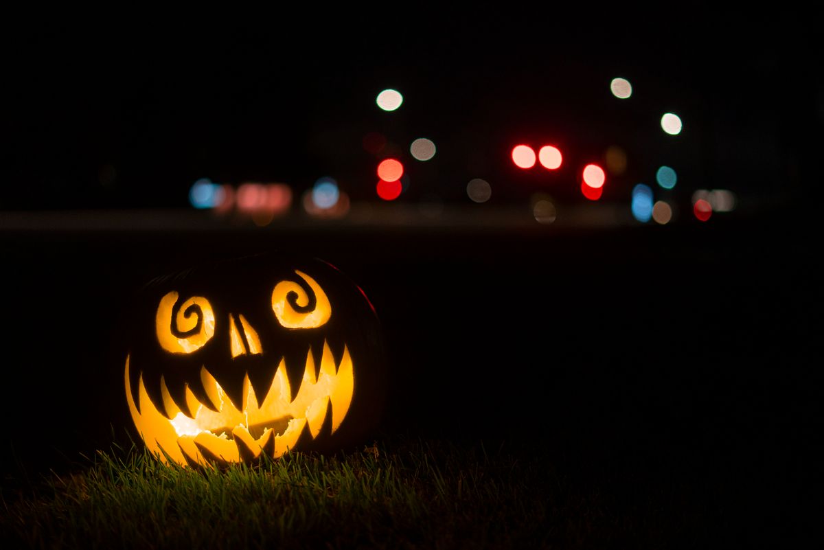 A glowing jack o'lantern with a spooky face on a dark night with bokeh city lights in the background.