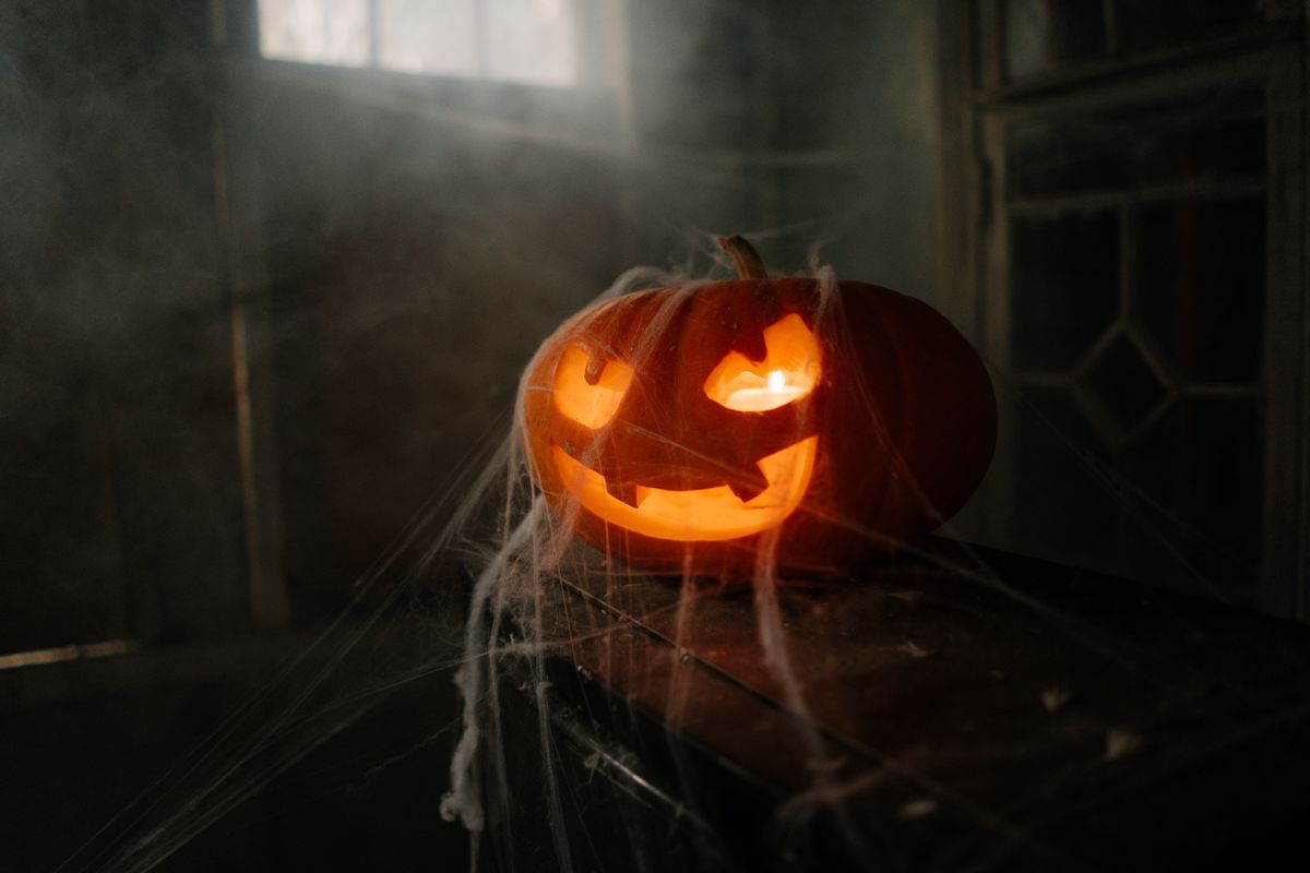 Carved pumpkin jack-o'-lantern illuminated on a spooky, cobwebbed indoor setting for Halloween.