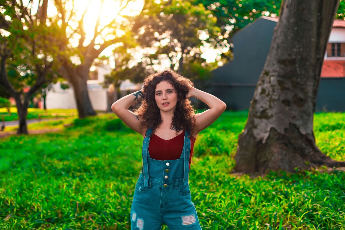 Portrait of a woman in overalls enjoying a sunny day in a lush green park in Bauru, Brazil.