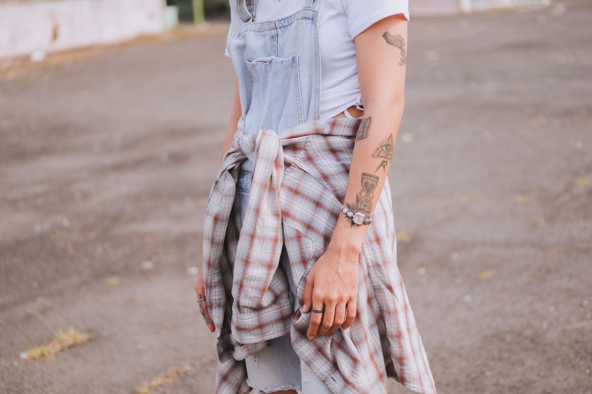 Close-up of a person in a denim jumper with tattoos, showcasing casual fashion style.