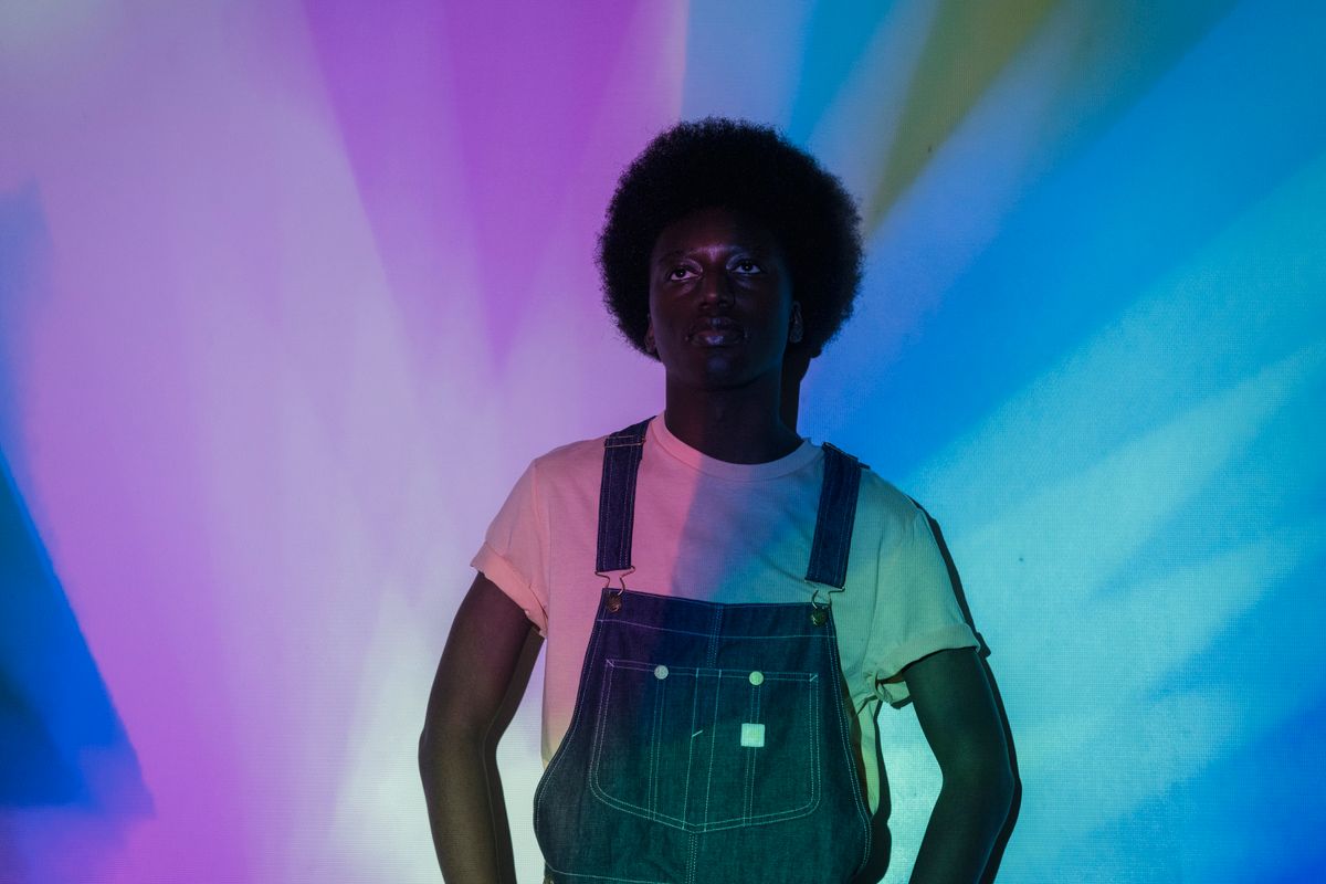 Young man in denim overalls against a colorful background with pastel tones.