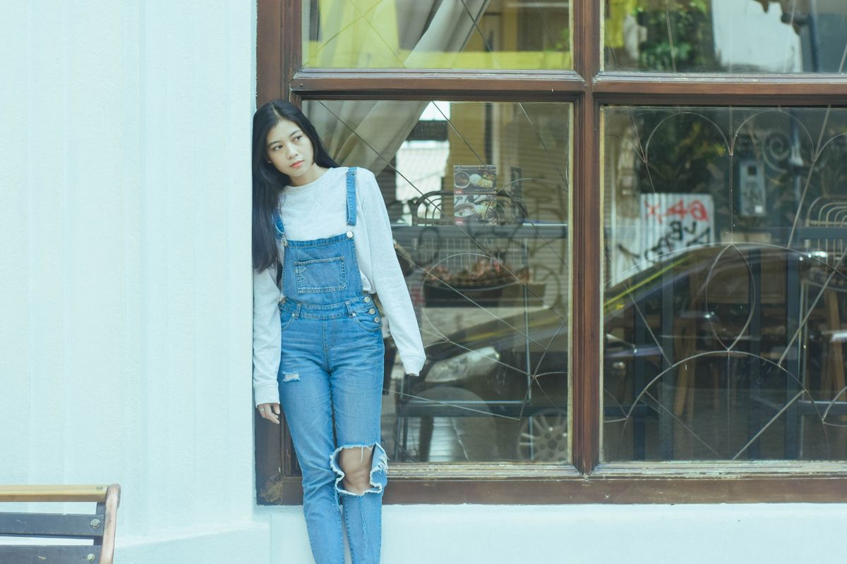 Woman in denim overalls leaning by a window, Jawa Barat, Indonesia.