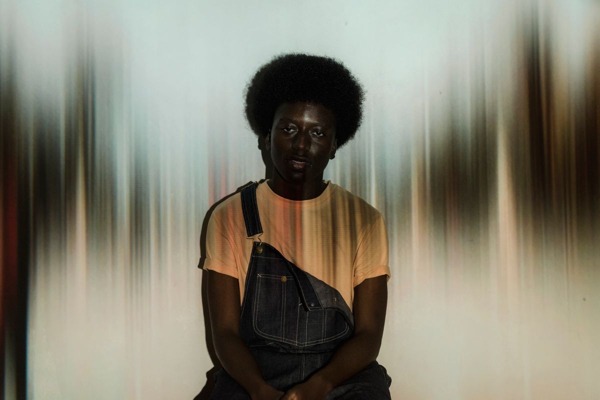 Portrait of a man with afro hair wearing denim overalls in a studio shoot with abstract background.