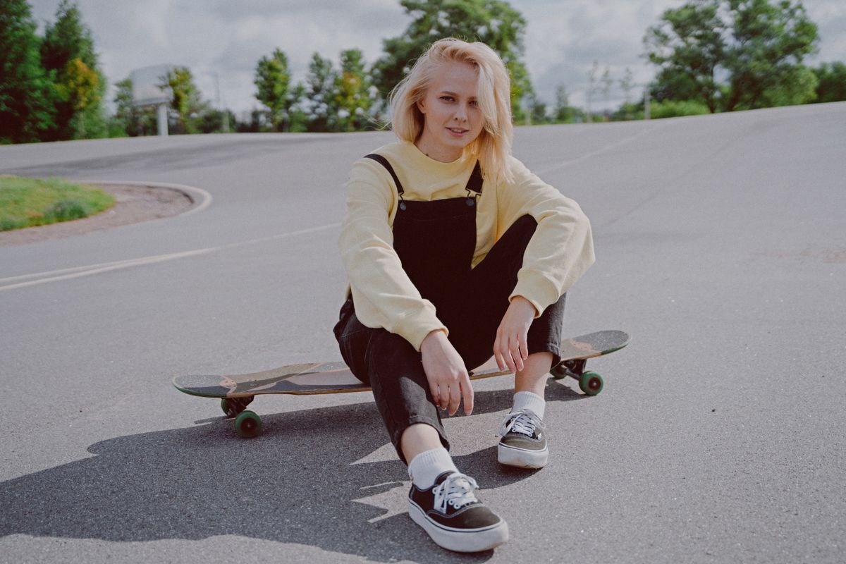Blonde woman sitting on a skateboard outdoors, embracing street style and leisure.
