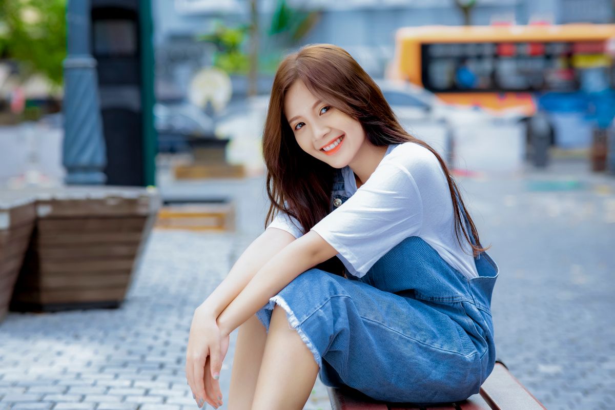 Portrait of a smiling young woman sitting outdoors in a casual outfit.