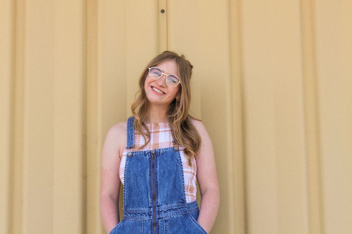 Portrait of a happy woman in casual denim overalls smiling outdoors against a yellow wall.