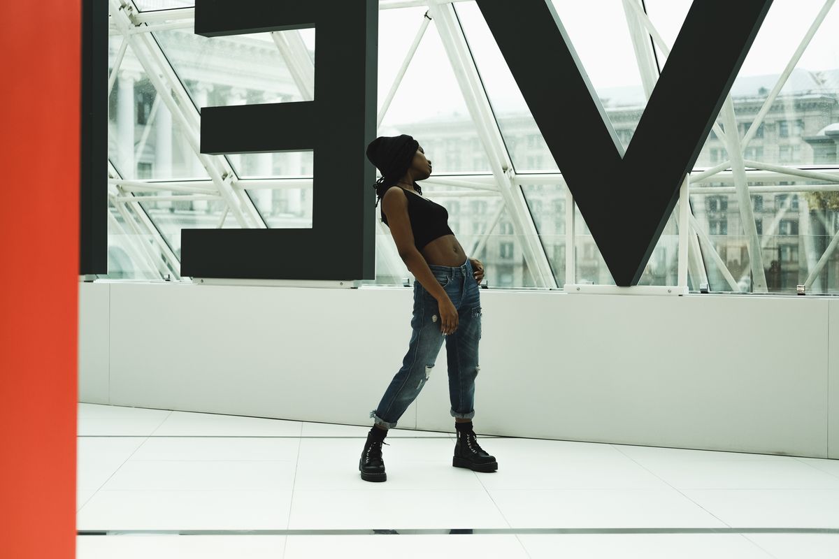 Fashionable woman in a crop top and jeans posing indoors with geometric architecture.