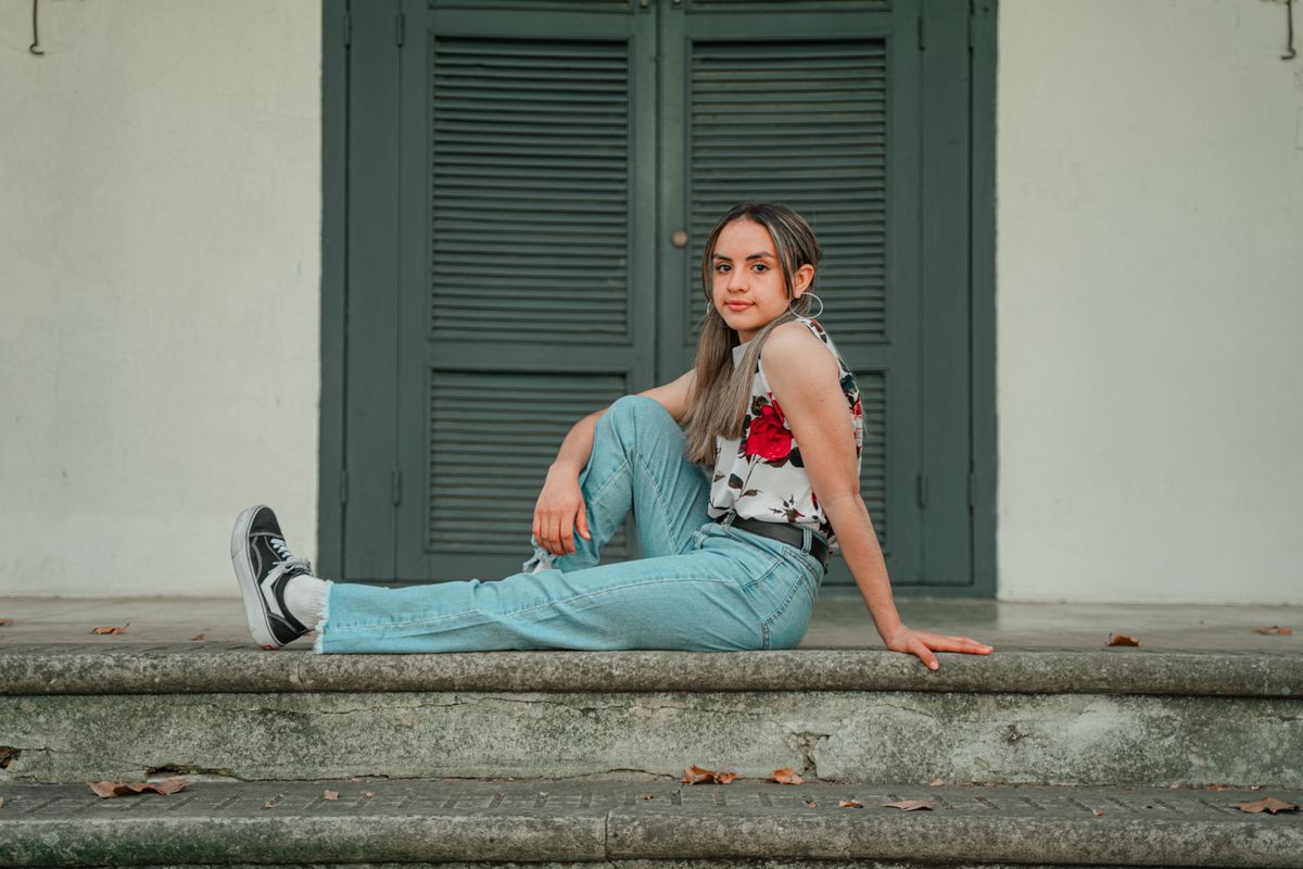 Chic young woman in denim and floral top seated on stairs, urban setting.