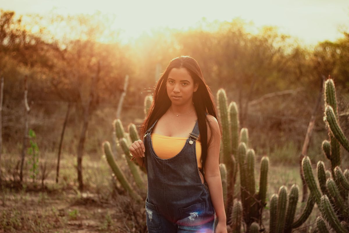 Woman in overalls standing in cactus field during sunset, creating backlit warm atmosphere.