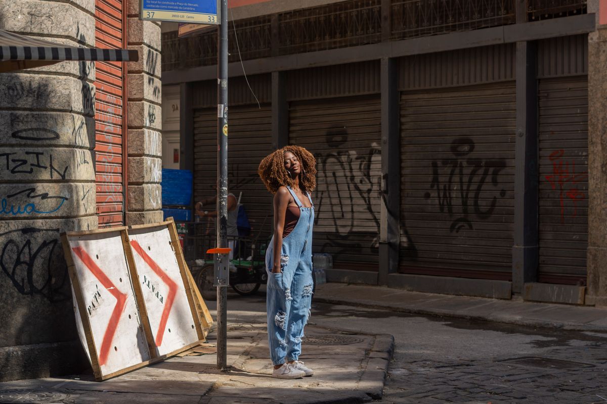 Woman standing confidently in urban street wearing denim overalls, surrounded by graffiti and city textures.