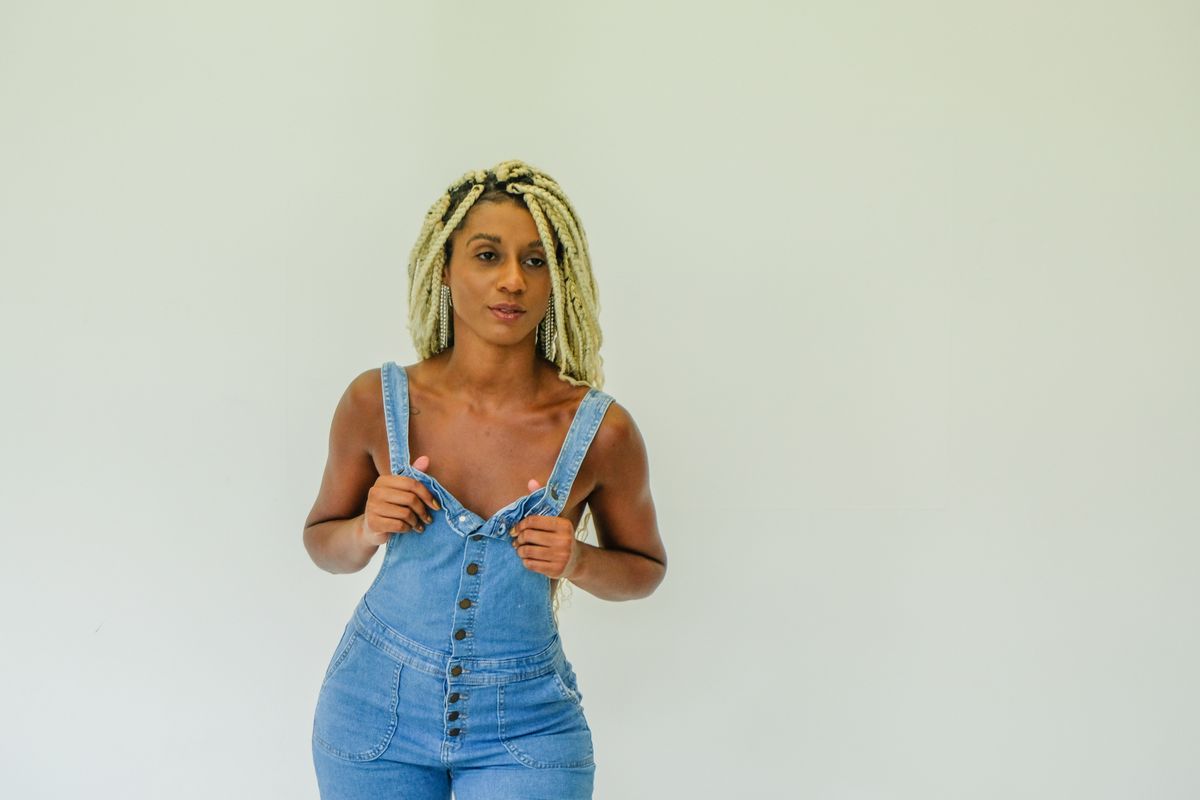 Stylish woman posing in denim overalls on a white background.
