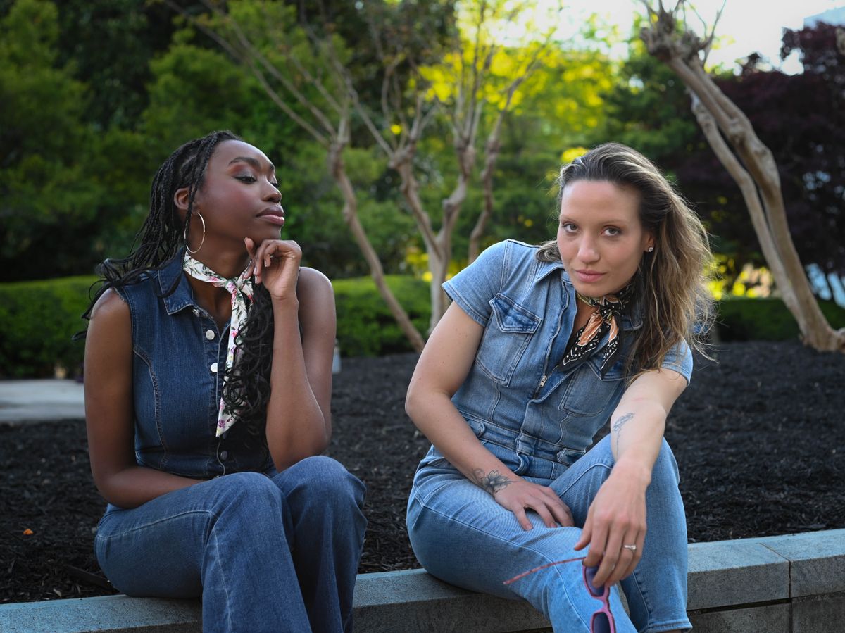Two women in denim outfits pose stylishly in a park, highlighting fashion and nature.