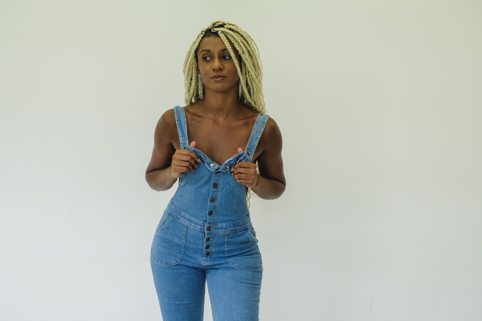 Portrait of a fashionable woman in denim overalls against a white background, exuding confidence and style.