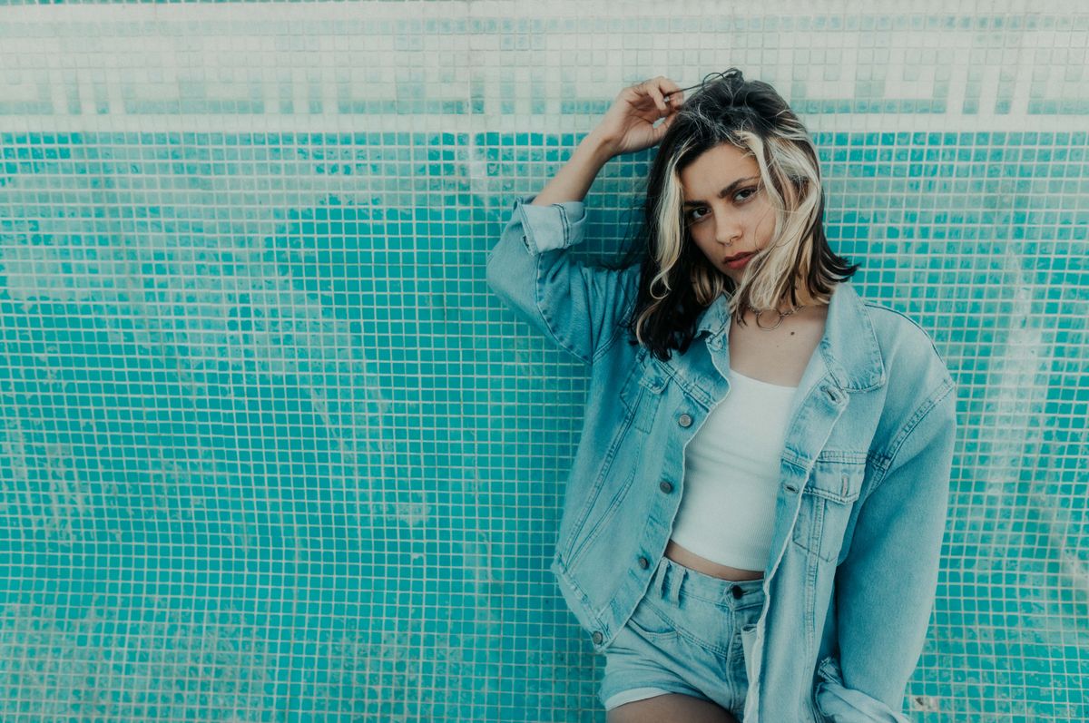 Stylish young woman in denim outfit posing against a blue mosaic wall, embodying modern fashion trends.