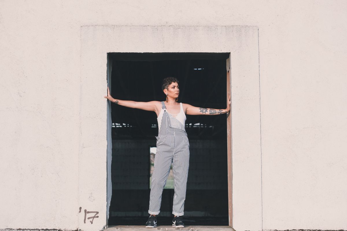 Stylish woman with tattoos wearing striped jumpsuit posing in an industrial doorway.