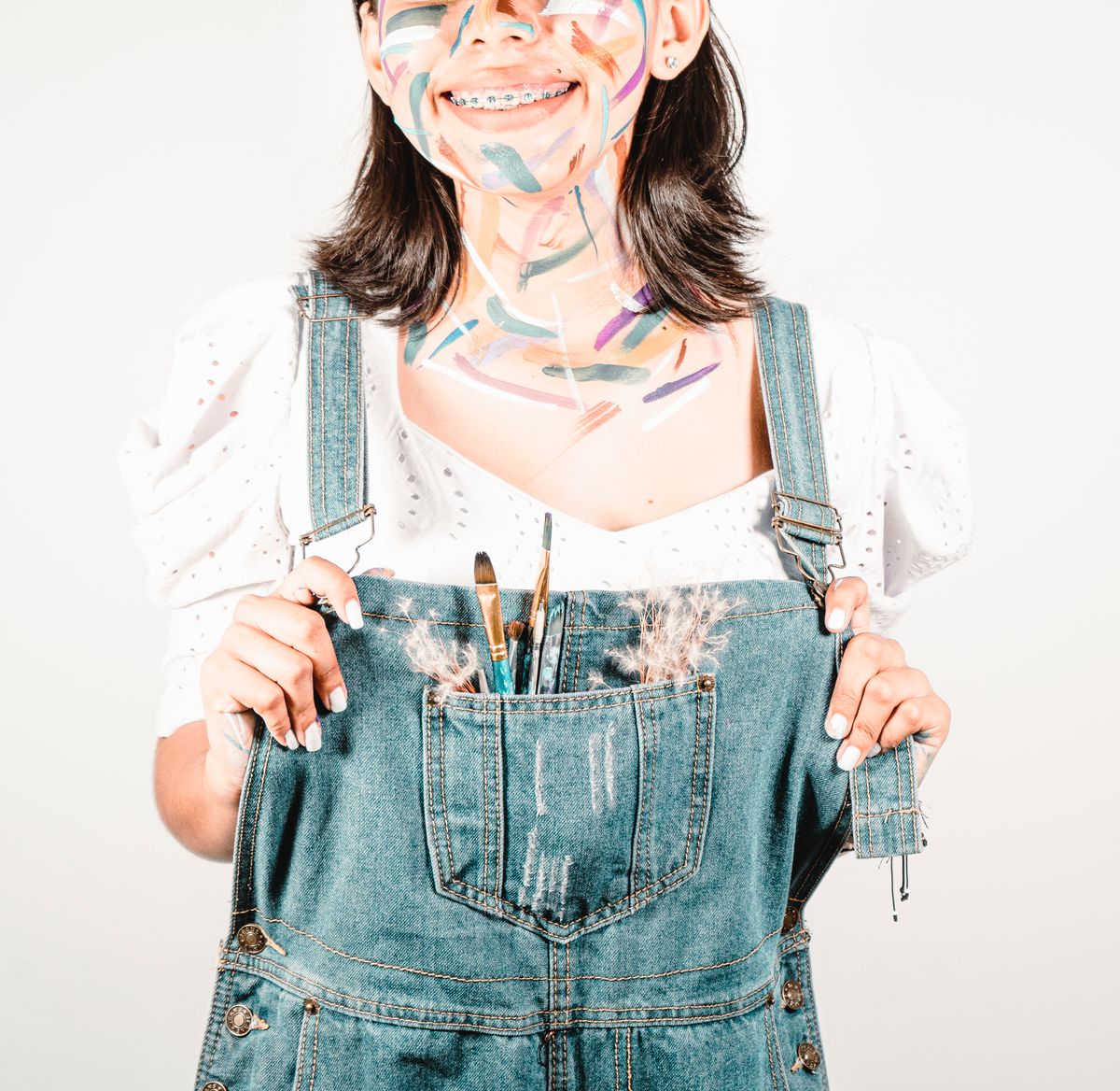 Young woman with painted face and denim overalls, expressing artful joy.