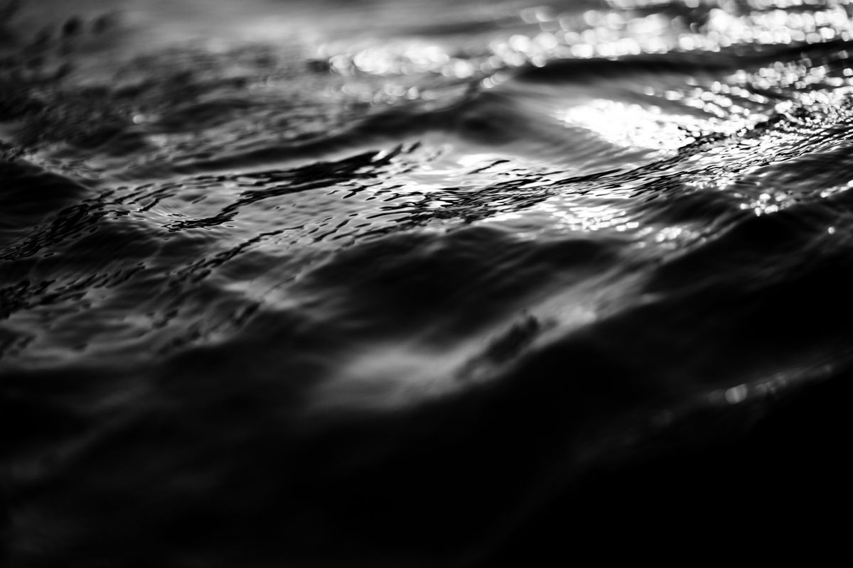 Black and white close-up capturing the textured movement of water with light reflections.