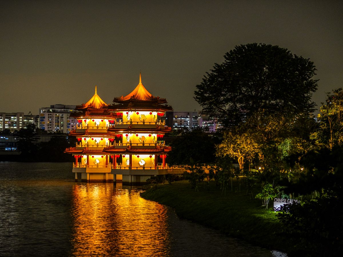 A glowing pagoda reflected in water at night in a serene Chinese garden setting.