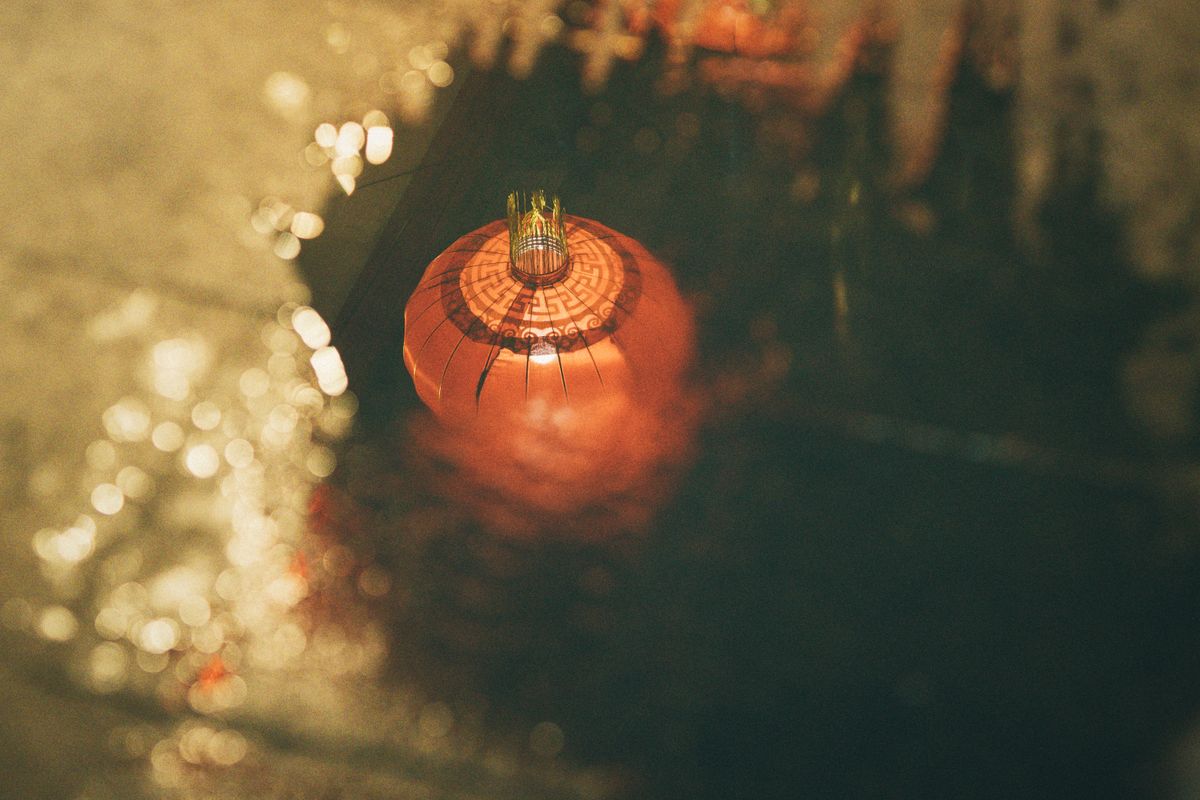 A red paper lantern reflecting in a water puddle at night, creating an artistic glow.