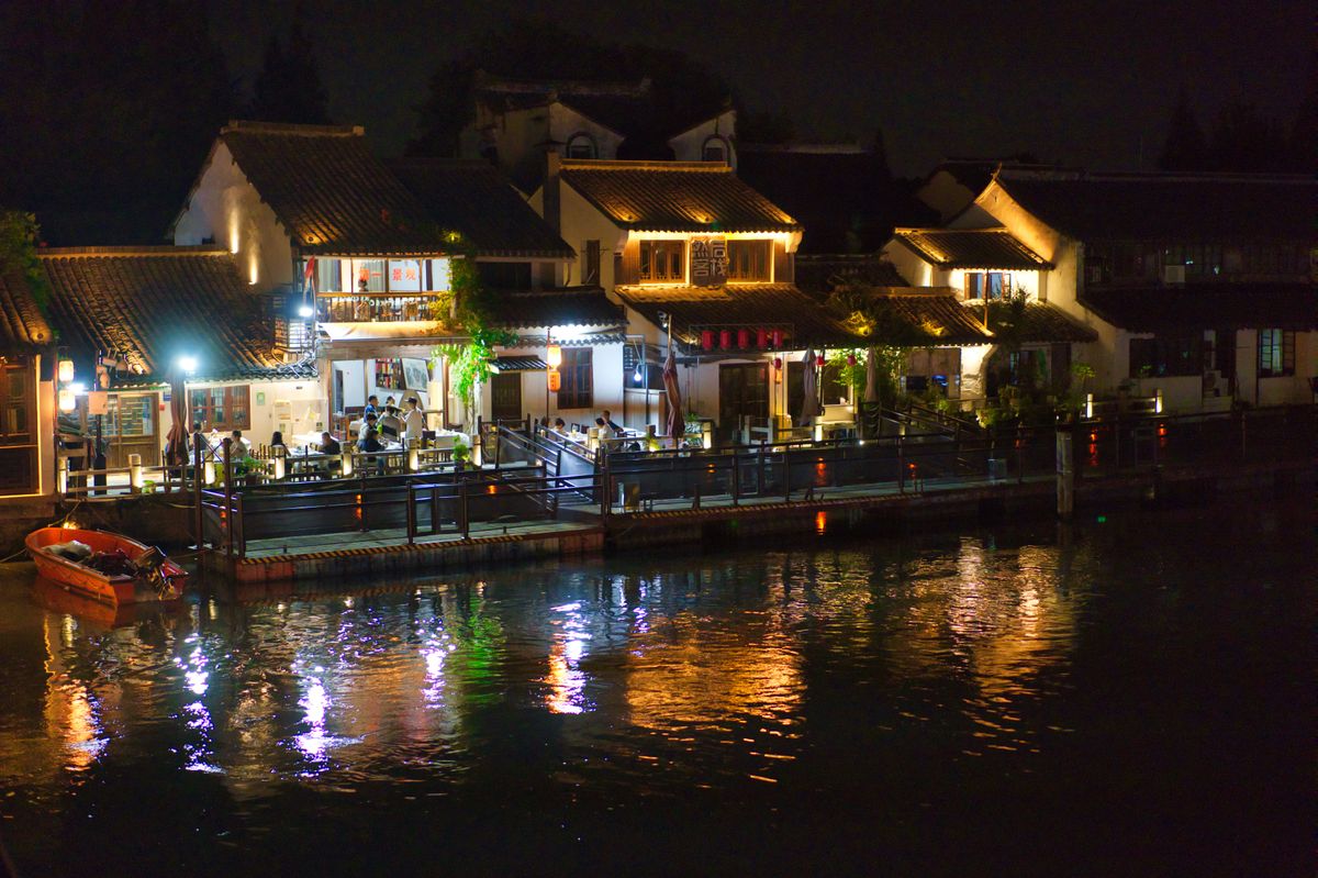 Charming illuminated riverside restaurants reflecting in the water at night, creating a serene atmosphere.