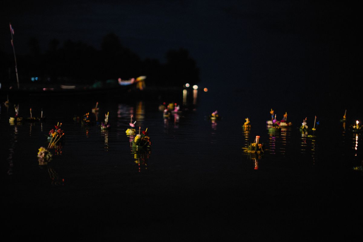 Beautifully lit krathongs floating on the water during Thailand's Loy Krathong festival at night.