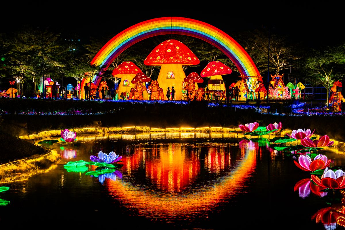 Illuminated mushroom houses and rainbow lights reflecting in a pond at night.