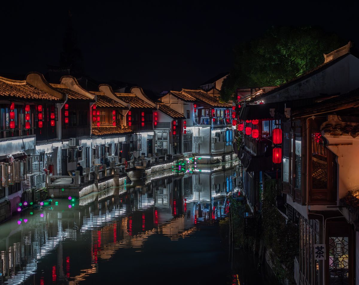 Illuminated Chinese canal buildings reflecting in the water at night.