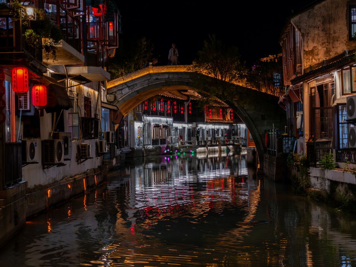 Scenic night view of illuminated canal and bridge in Suzhou, China, reflecting vibrant lights.