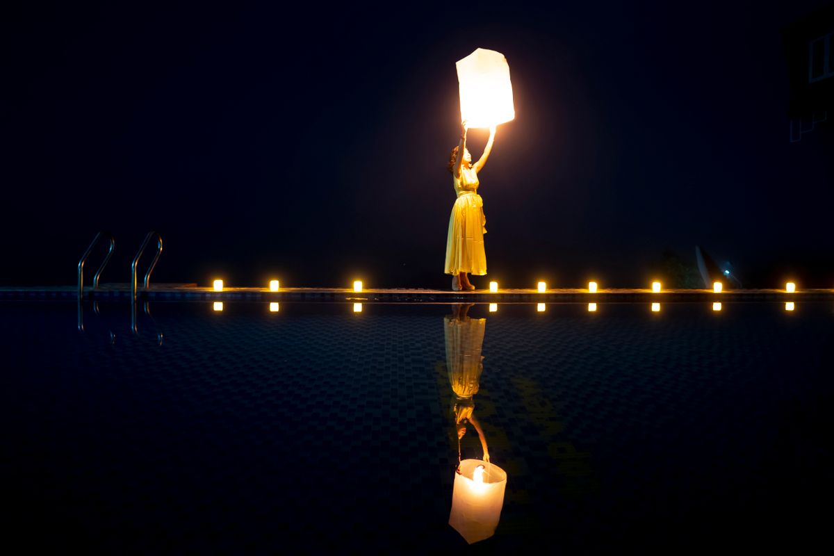 A woman releases a lantern by a pool surrounded by candles at night.