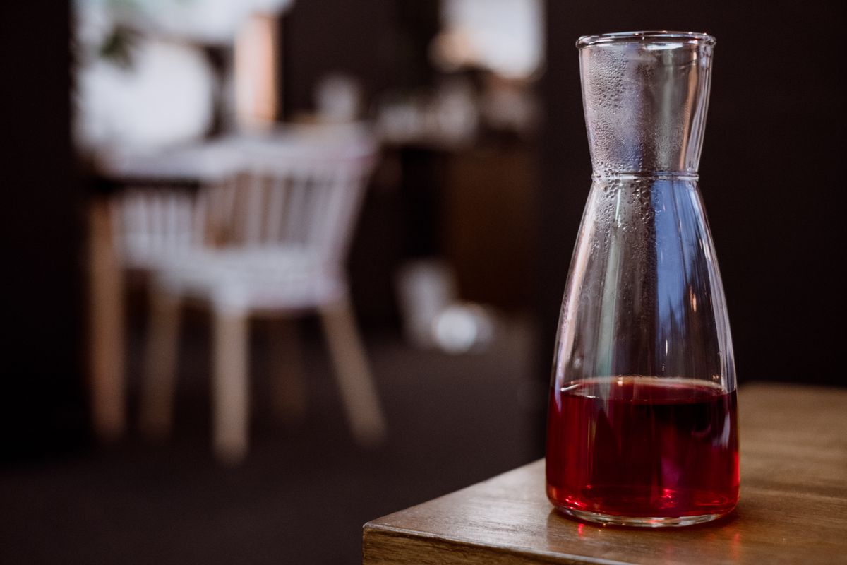 Close-up of a glass carafe filled with red liquid on a wooden table in a cozy indoor setting.
