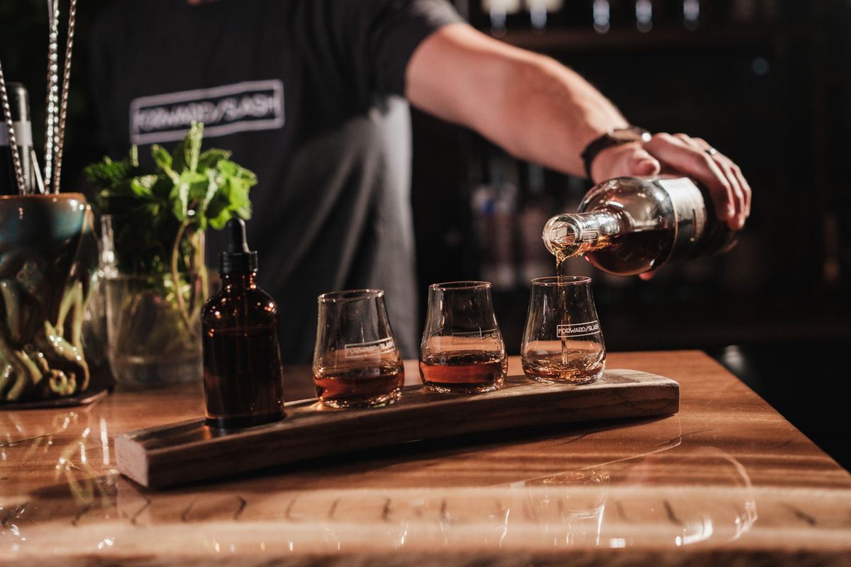 Bartender pouring whiskey samples in a rustic bar setting, showcasing drinks and atmosphere.