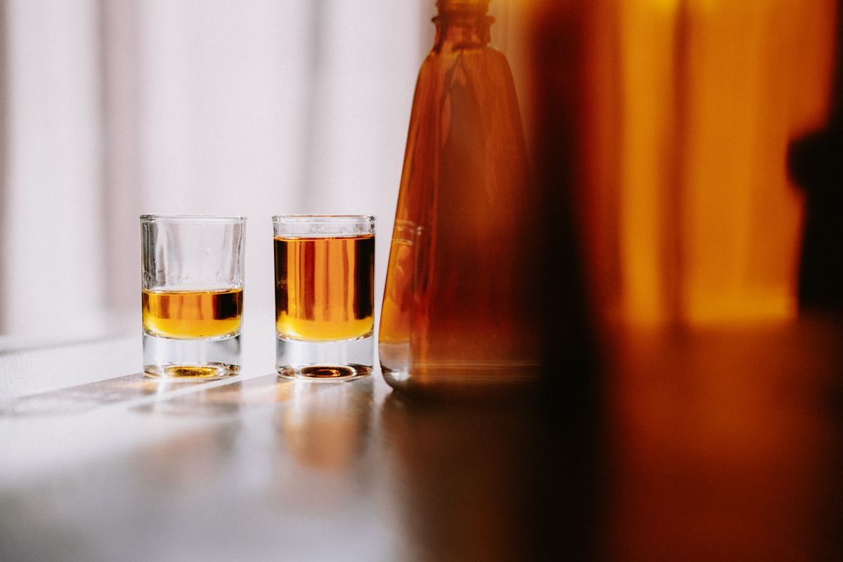 Two whiskey glasses with amber liquid and a bottle on a sunlit table for a sophisticated setting.