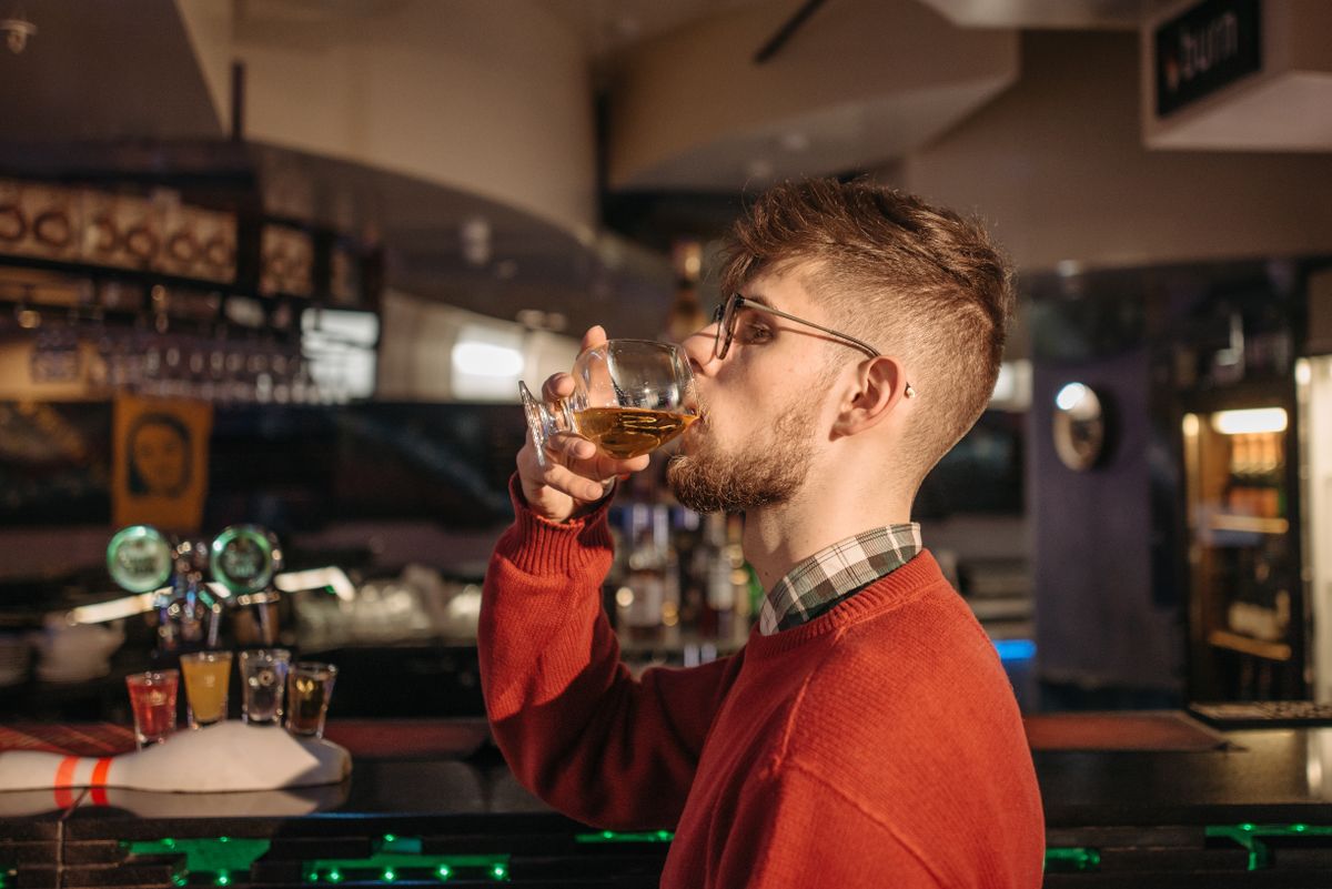 Young man savoring a drink in a stylish bar setting, surrounded by warm lighting.