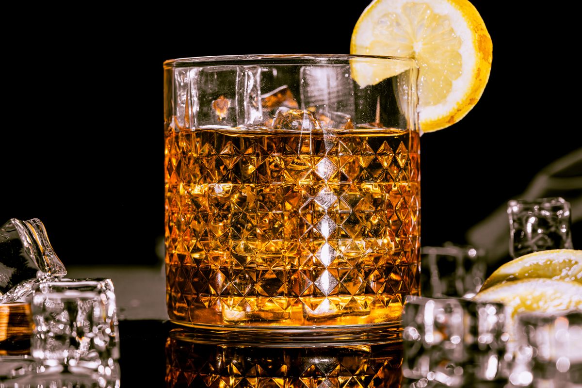 A classic whisky glass with intricate design filled with whisky, garnished with a lemon slice and surrounded by ice cubes.