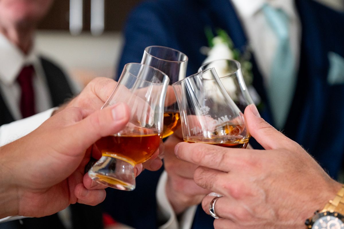 Close-up of businessmen toasting with whiskey glasses at a formal event.