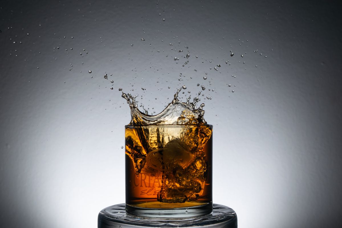 Dramatic image of whiskey splashing in a glass with ice on a reflective surface.