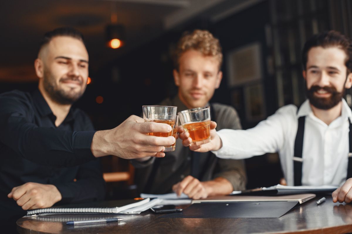Three smiling men toasting with whiskey glasses in a relaxed indoor setting.