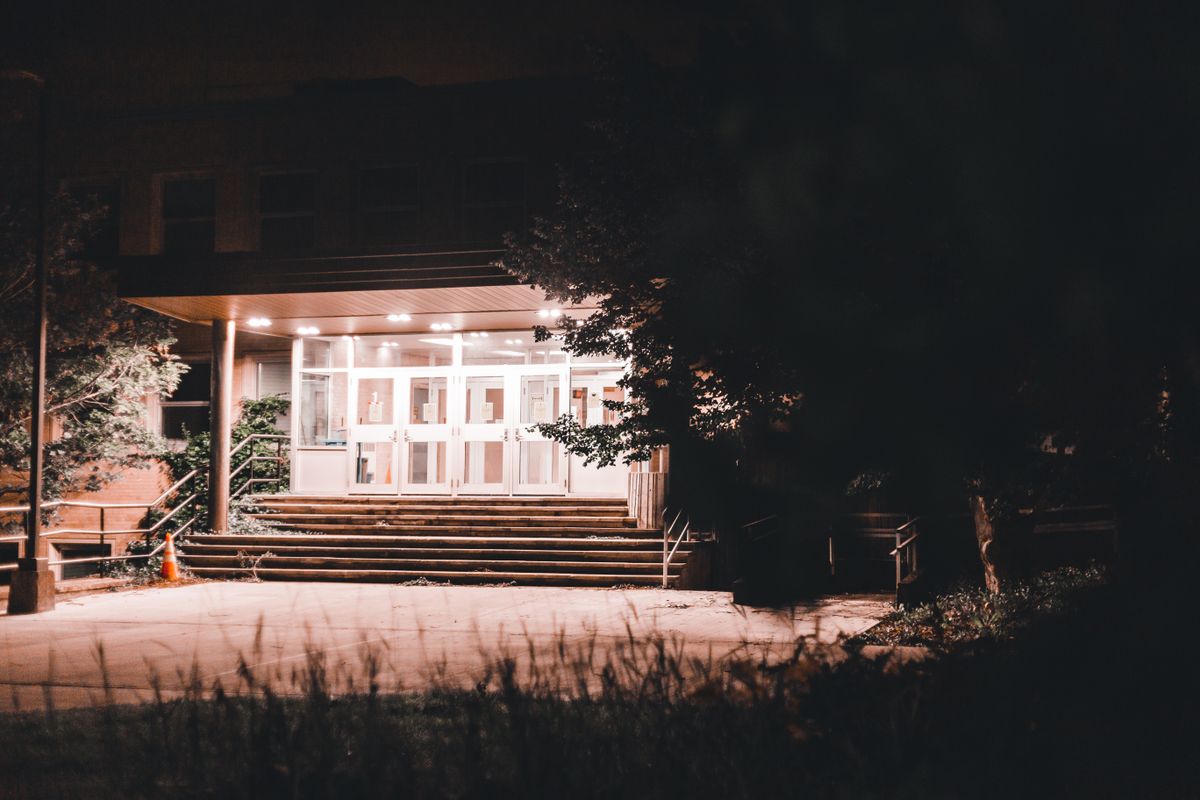 Entrance of a building lit at night, showcasing modern architecture and stairs.