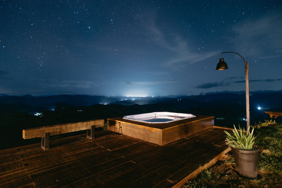 Relaxing outdoor jacuzzi under a starry sky with distant city lights in Santa Teresa, Brazil.