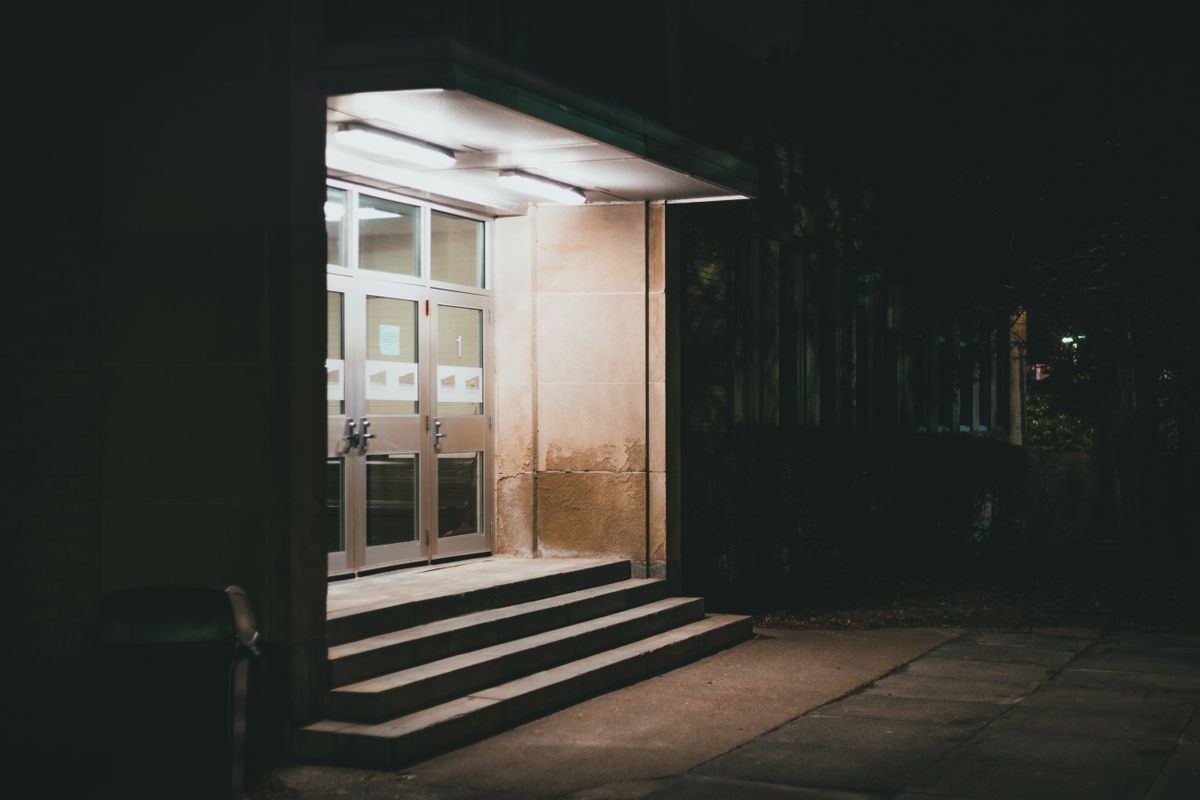 Moody image of a building entrance with stairs illuminated by night lights.
