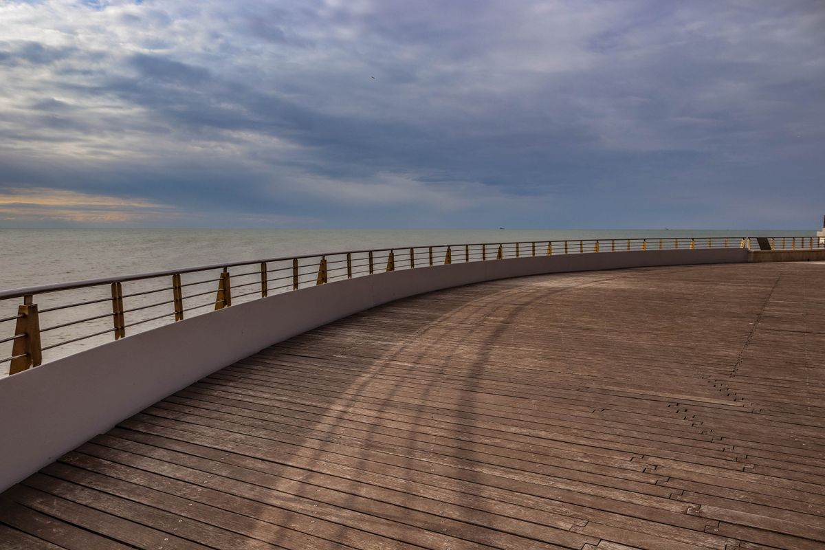 Beautiful outdoor scene of an ocean view with an expansive wooden deck and railings at sunset.