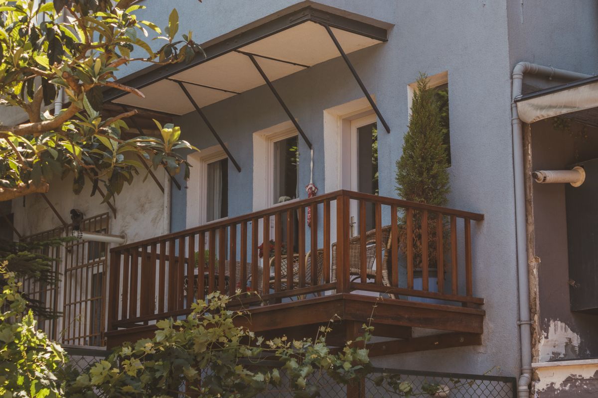 A small balcony with wooden railing, plants, and cozy seating enhances a tranquil urban outdoor setting.