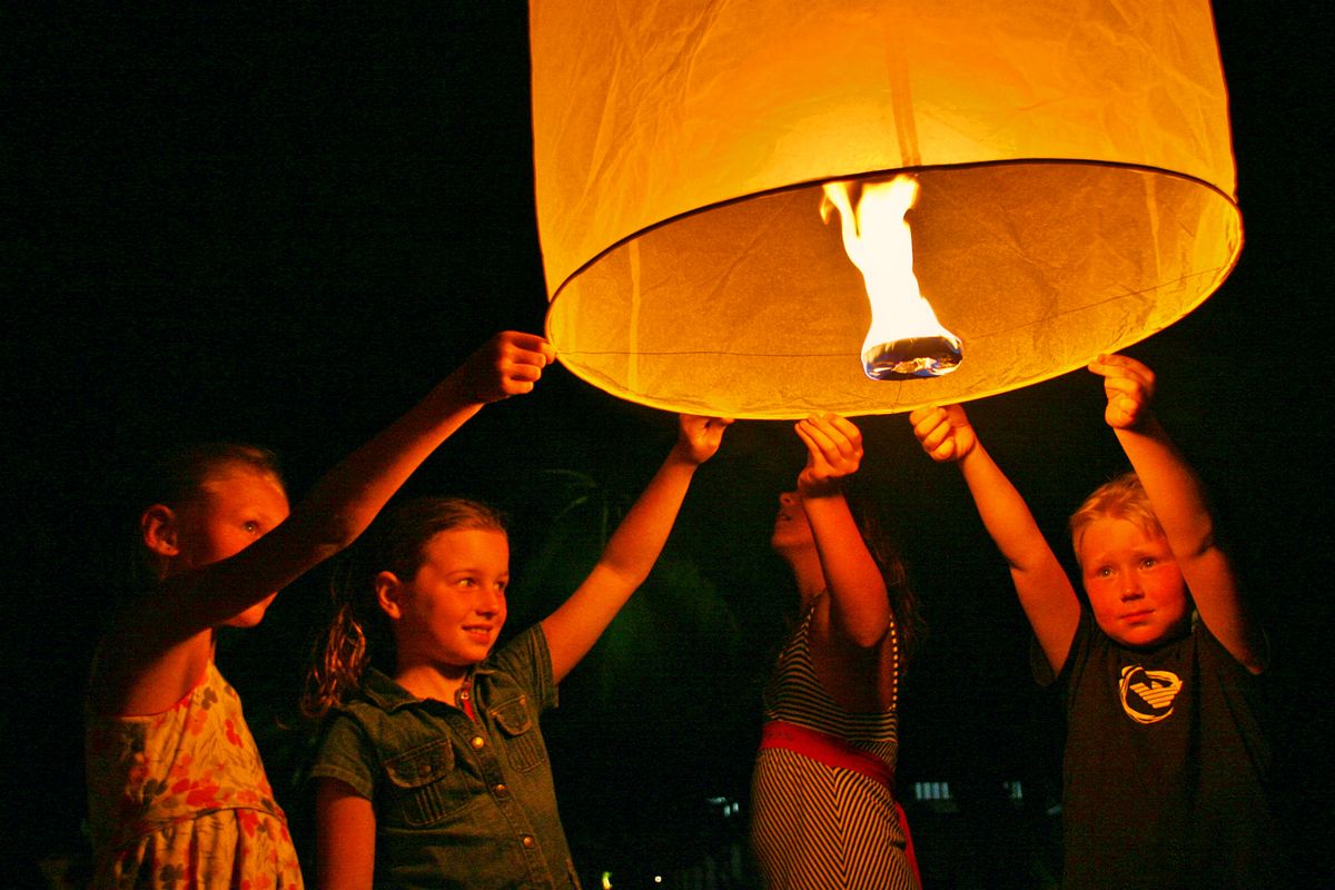 Kids joyfully release a glowing Thai lantern into the night sky in Phuket, Thailand.