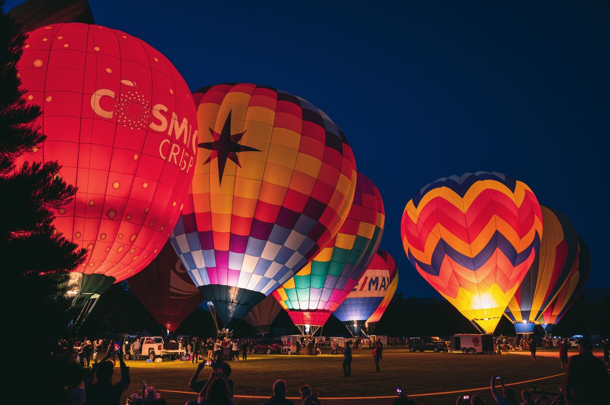 Colorful hot air balloons illuminated at a nighttime festival, creating a lively outdoor scene.