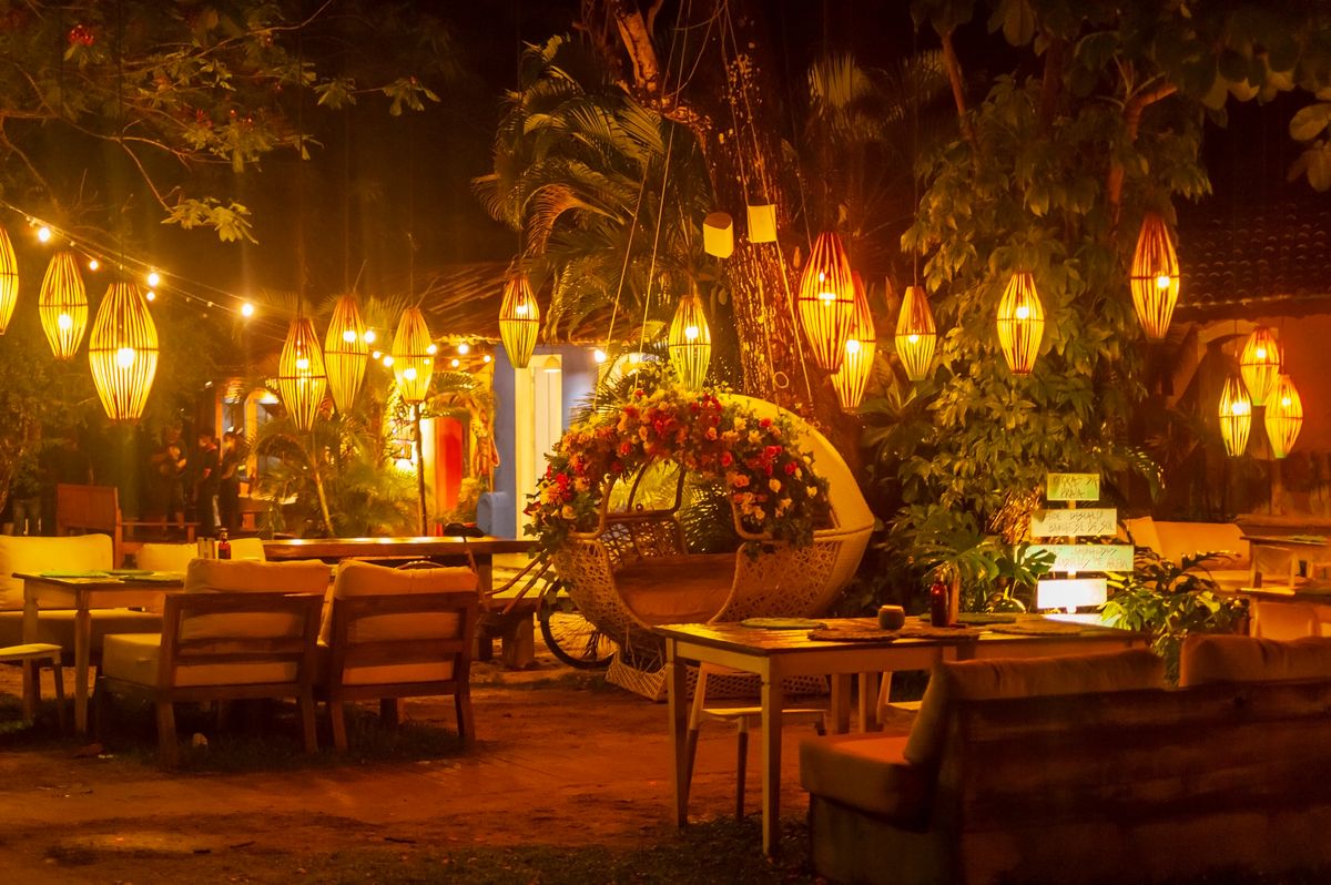 Warmly lit outdoor restaurant with cozy seating and hanging lights at night.