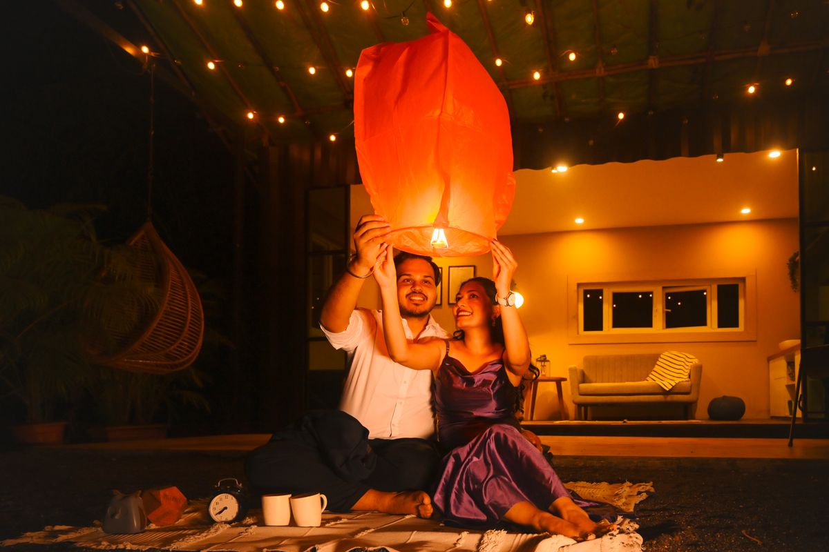 Couple releasing lantern in a cozy outdoor setting with warm lighting, capturing a romantic moment.